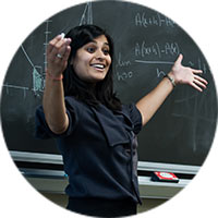 A faculty member in front a chaulkboard smiles and raises her arms emphatically