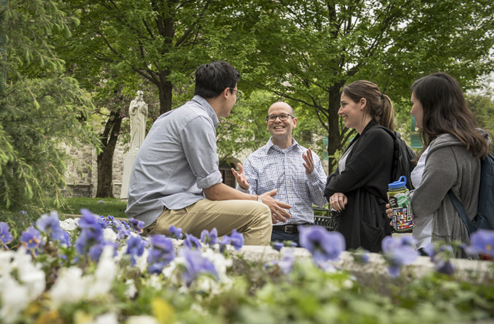 Students chatting with a Loyola administrator outside on the grassy Quad with flowers in the foreground