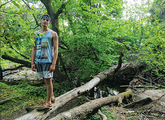 Student balancing on a fallen tree trunk reaching across a creek