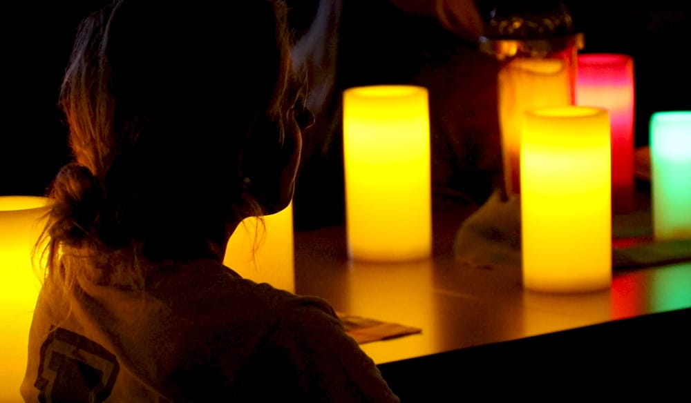Yellow, red, orange, and green candles glow and light up a silhouette of a student's face