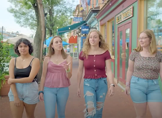 Four female students walking past shops in a quaint neighborhood near campus