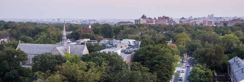 The steeple of Alumni Memorial Chapel poking out of the tree line, overlooking N Charles Street and the city on the horizon