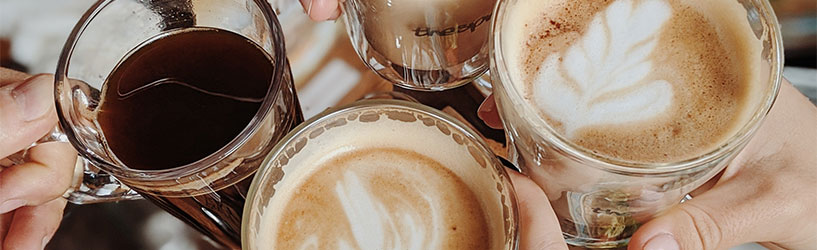 Hands holding their different lattes in glasses together for a closeup photo
