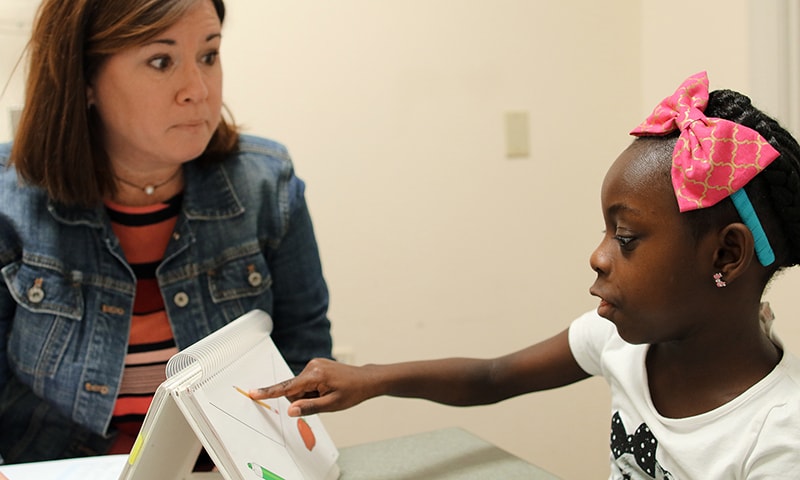 A young girl points at a picture while working with a Clinical Centers staff member