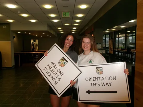 Two happy students hold signs leading to orientation