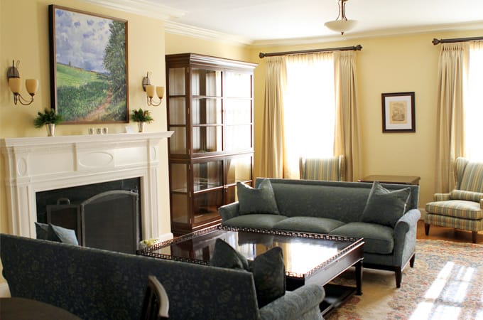A tan room filled with blue couches, a fireplace, and other furniture. A painting of a field hangs on the wall.