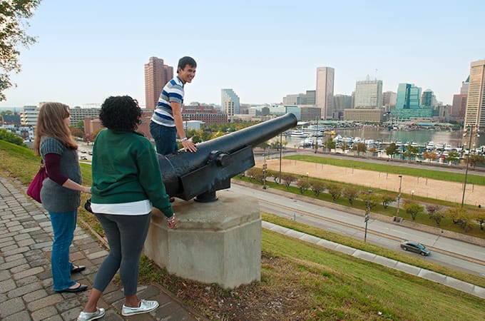 Students near an old cannon, looking toward Chesapeake Bay and downtown Baltimore