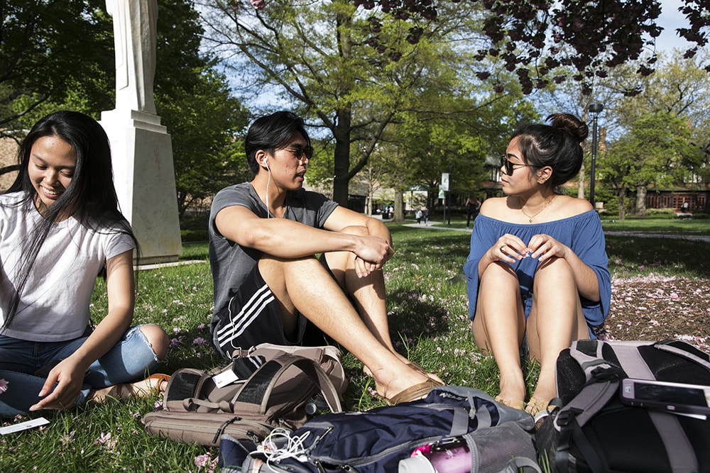 Students sitting on the grass conversing during a sunny day on the quad