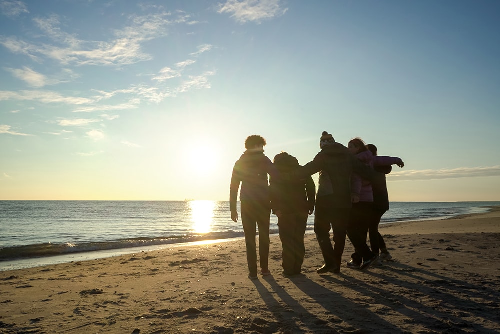 A silhouetted group of students with their arms around each other near the waterline on a beach