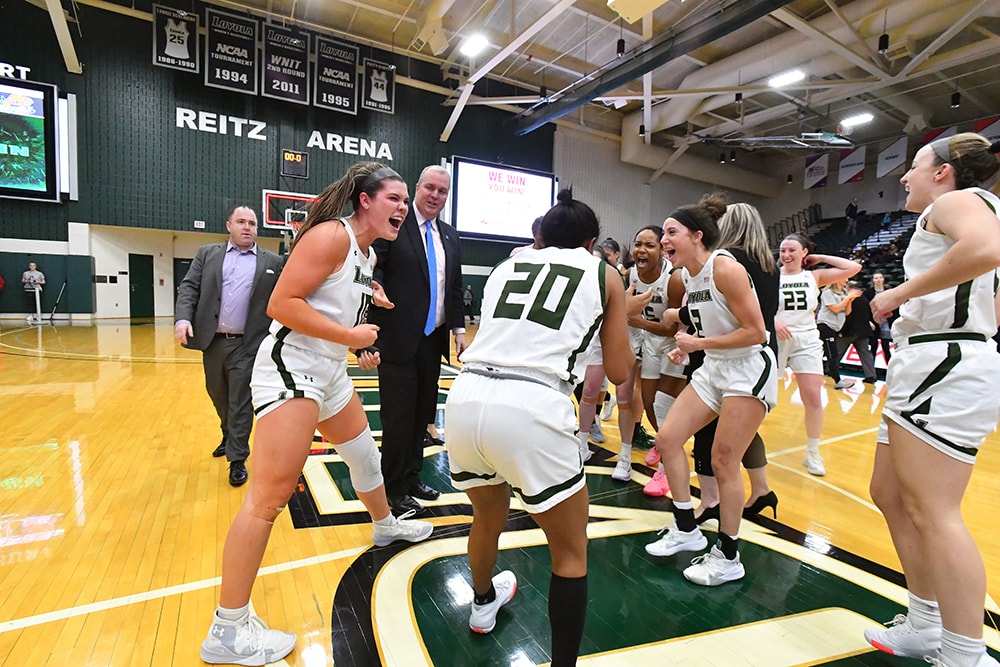 Members of Loyola's women's basketball team in a group celebration on the court of Reitz Arena