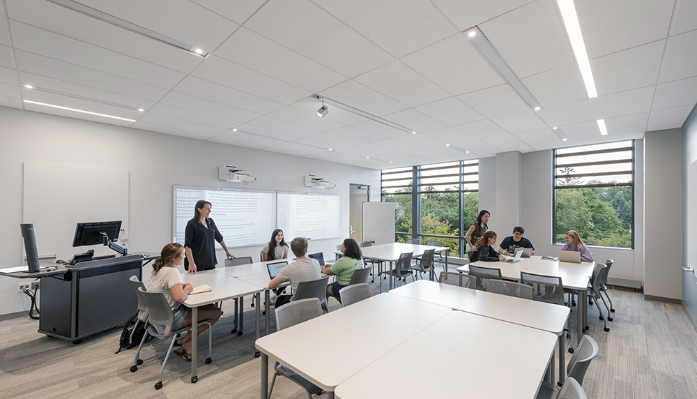 Students and a professor in a modern classroom with large white tables