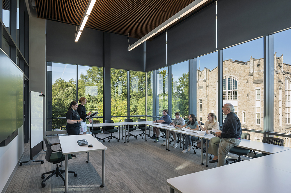 Students and faculty sit in a classroom with glass walls, showing trees and Jenkins hall outside