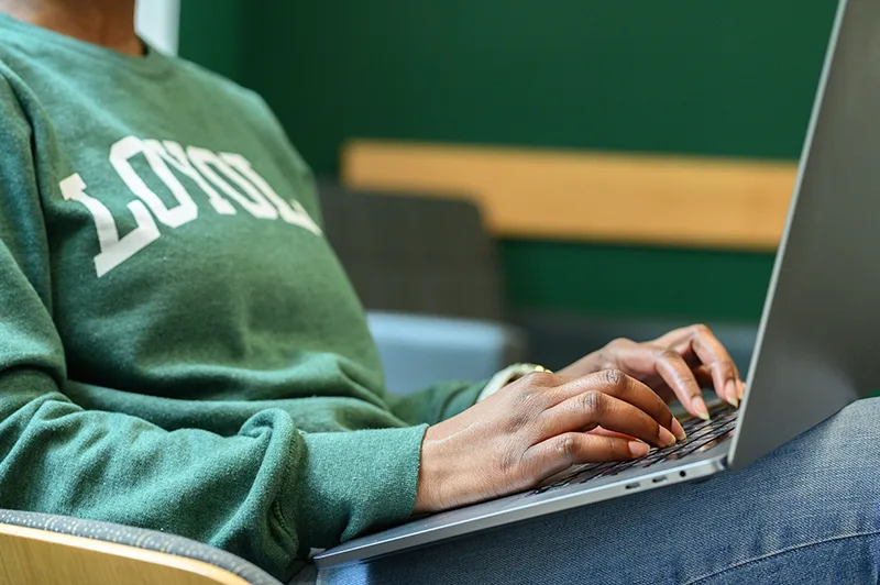 A student wearing a green Loyola shirt types on a laptop