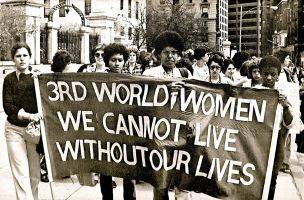 a black and white photo of four women holding a banner in a crowd