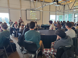 David Carey presenting to large crowd sitting around round tables eating lunch