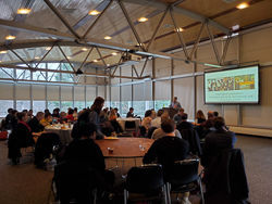 David Carey presenting to a large crowd eating at tables