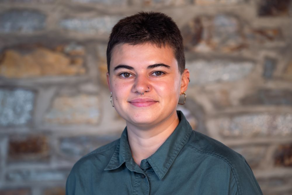 Headshot of Sophie Ragot wearing a green collared shirt with a stone wall in the background