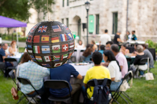 A globe with country flags is in the foreground with a student luncheon in the background