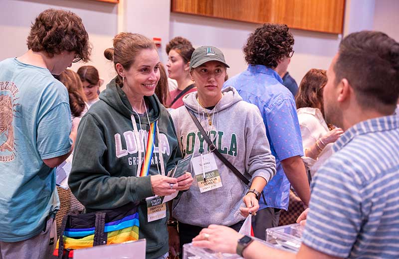 Parent and student chatting with a Loyola staff member at a table during a family event