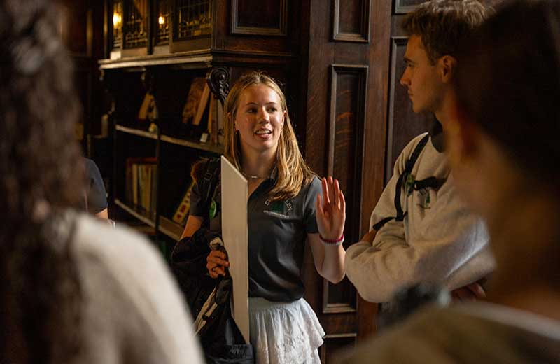 Student tour guide talking with a small tour group near a large ornate wooden bookcase