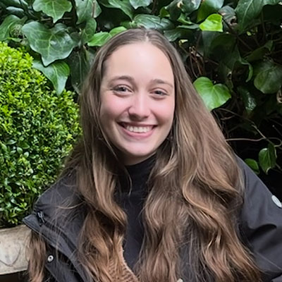 Julia smiling in front of a wall of vibrant green plants