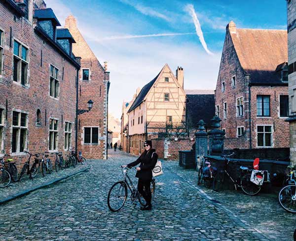 Student standing with a bike in the middle of a cobblestone street in an old town