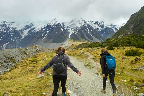 Two students with arms stretched to the sides running toward a huge mountain range