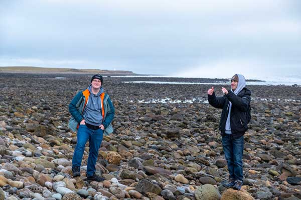 Two students standing atop a vast plane of rocks and stones by the ocean