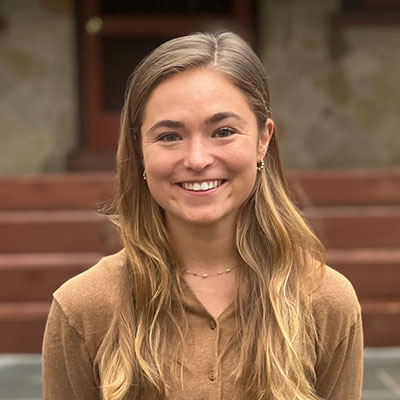 Katie West smiling in front of a large stone porch