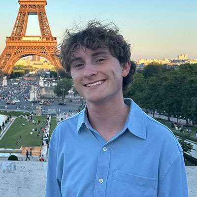 Alex smiling with the Eiffel Tower in the background on a clear day