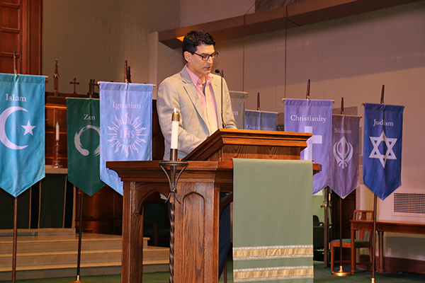 Dr. Daniel Castillo, HARPS 2024 keynote speaker giving his address in front of interfaith flags