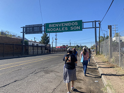 Group of students walking across a "Welcome to Nogales" sign during the Kino Border Immersion