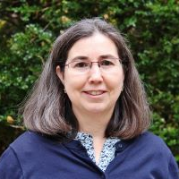 Ana Gomez-Perez from the shoulders up wearing a blue shirt in front of a green background