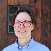 Jennifer Holt with red glasses standing in front of a brown wooden door
