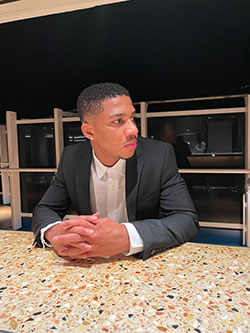 AJ Tolentino, sitting at a counter in a business suit, hands folded