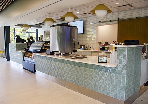 The light green, tile counter of the Green & Grey cafe with a digital menu board and glass pastry display
