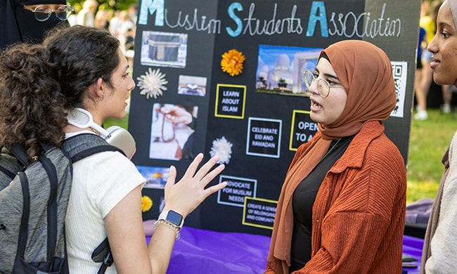 A young Muslim woman with glasses and a hijab speaks with a fellow student