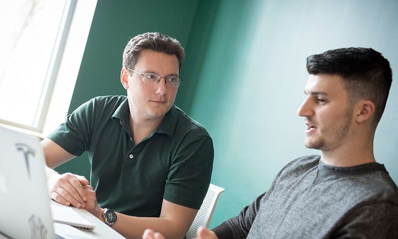 A male student speaking with a faculty member in front of a laptop