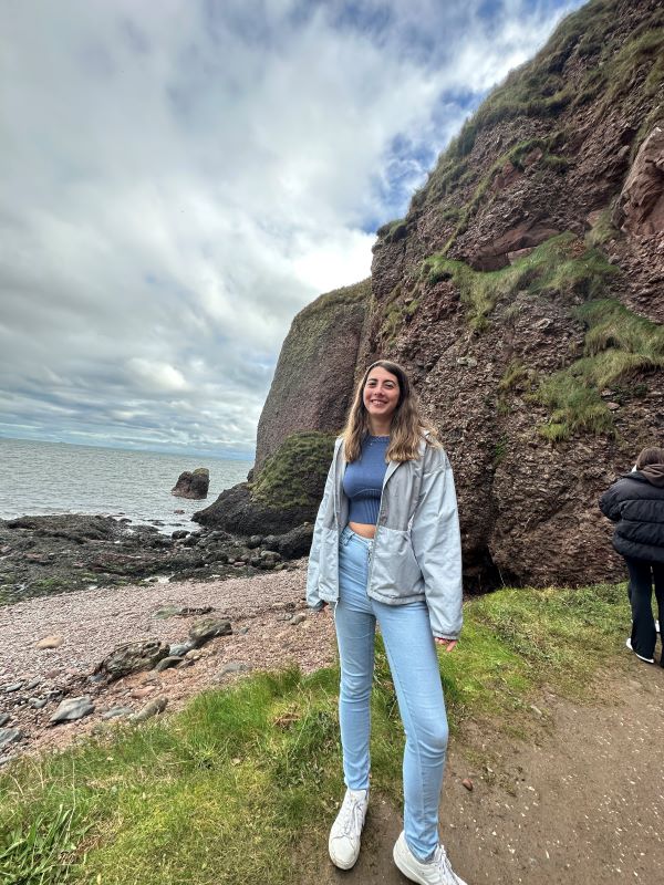 A student standing in front of a rock and beach