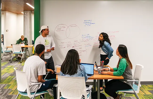 Students working together around a table and using a large whiteboard