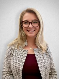 Sydney Quantock smiling in a maroon shirt with a cream plaid blazer. White background