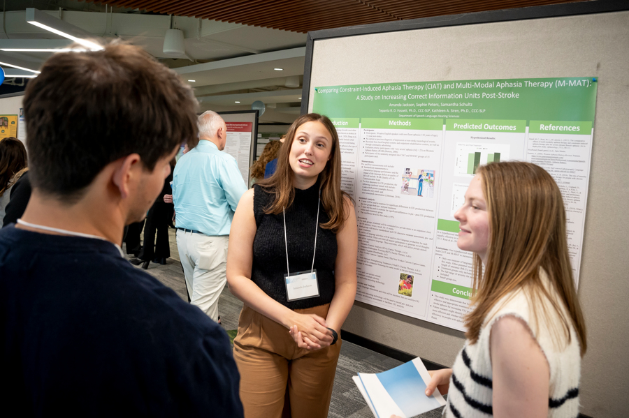 Two graduate students present their poster to a visitor at Emerging Scholars 2024