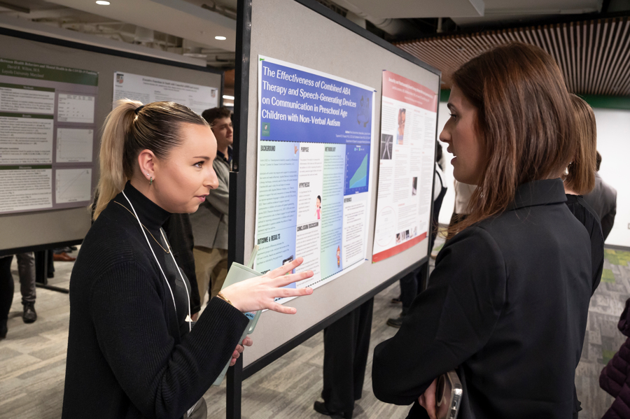 Presenter alongside poster explains her research to visitor at Emerging Scholars 2024