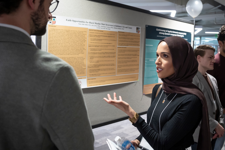 Presenter discusses research in front of poster at Emerging Scholars Loyola University Maryland