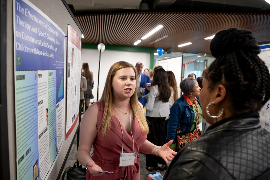 Presenter discusses research poster with visitor at Emerging Scholars 2024