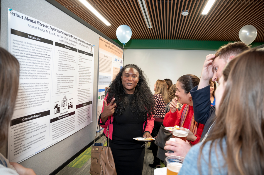 Graduate student gestures in front of poster with visitors at Emerging Scholars 2024