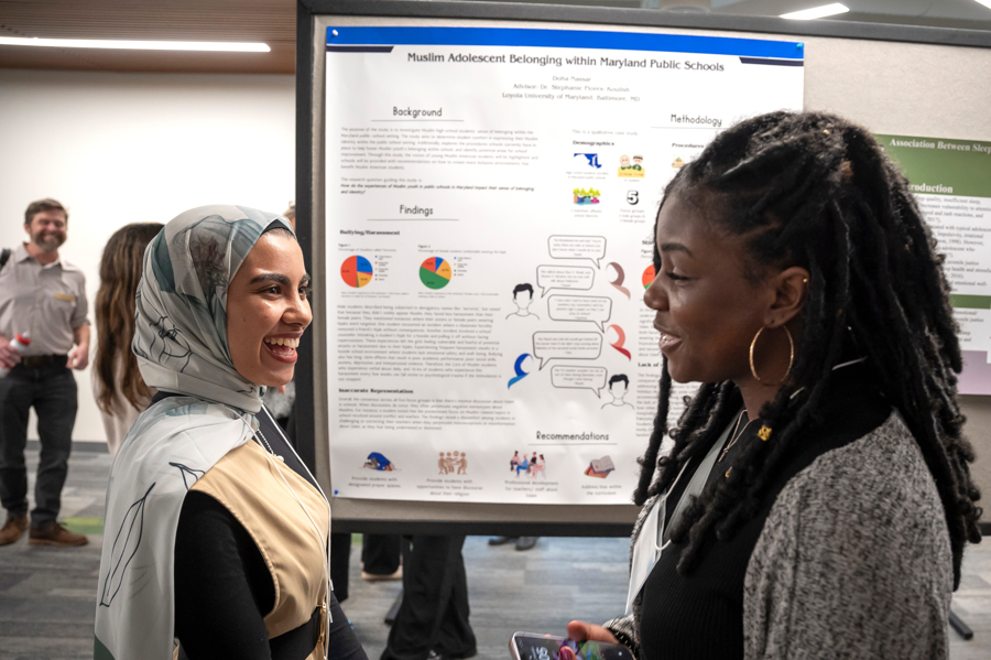 Two graduate students smiling in conversation in front of poster at Emerging Scholars poster session 2024