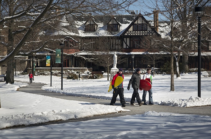 Students carrying sleds walking around a snow-covered campus
