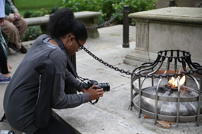 Student kneeling while filming a flame at a memorial in Philadelphia, Pennsylvania