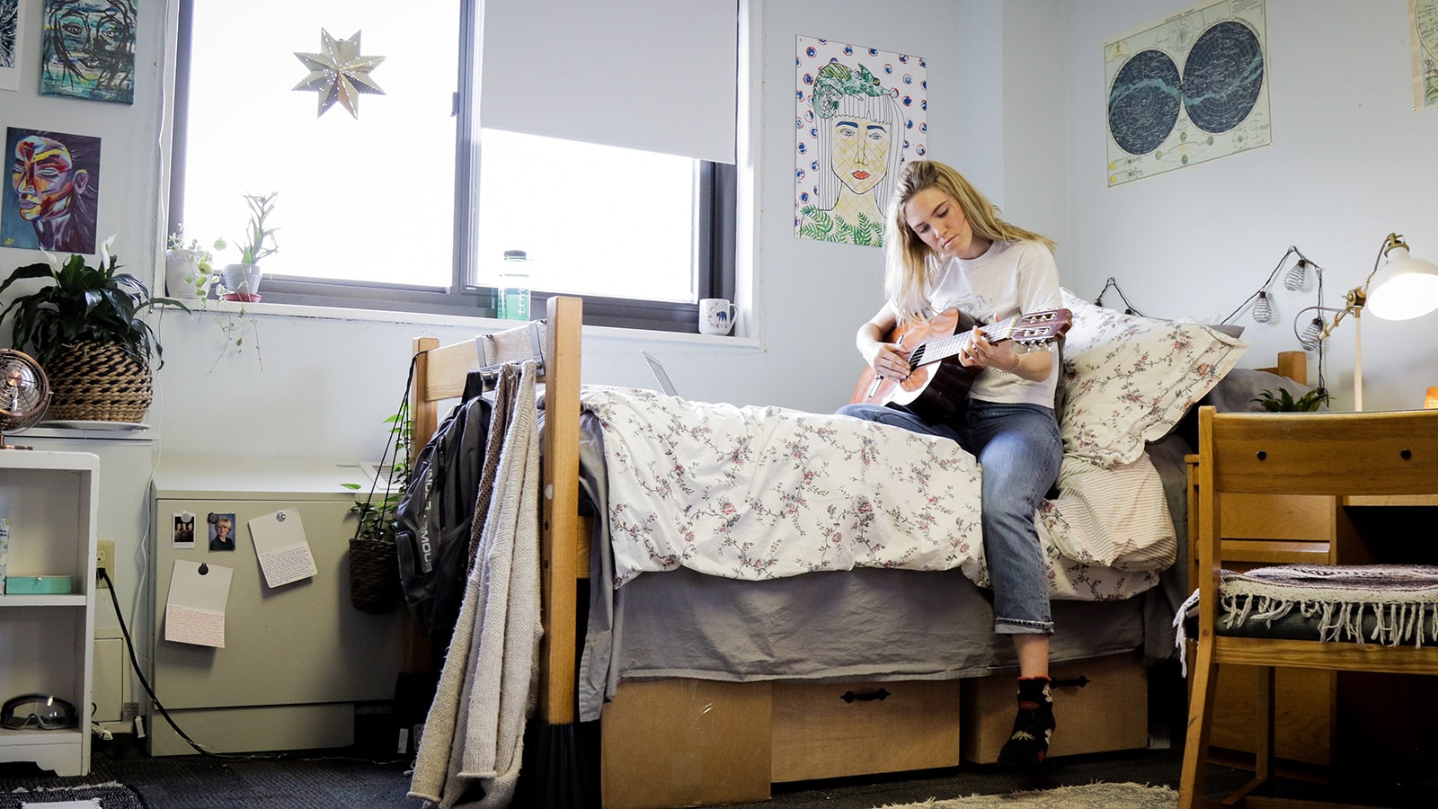 Student sitting on dorm bed playing guitar